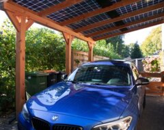 Blauwe auto onder houten carport met zonnepanelen